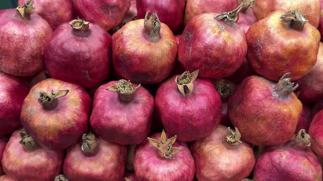 Ripe pomegranate fruits piled together, vibrant close-up of red skins and dried crowns, market stall arrangement with rustic