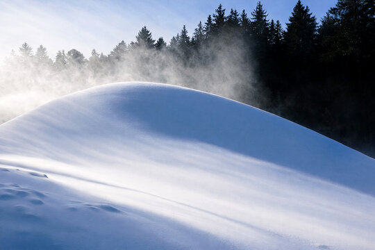Beautiful winter landscape of a snow covered hill with sun rays and mist