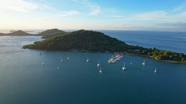 Aerial drone footage of Gili Gede touristic paradise island, West Sekotong, Lombok island, Indonesia, at golden sunset,   with many white mast boats at anchor, a pier, quiet sea bay, Gili Layar behind