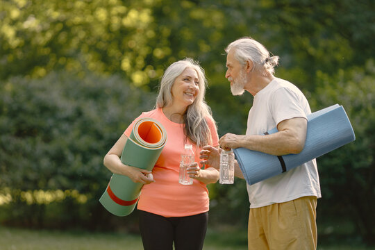 Senior couple with exercise mats standing at park and talking