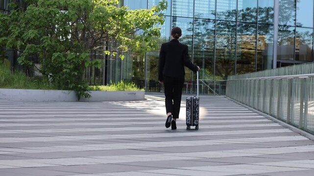 Business traveler walks down a path with a suitcase in an urban area during the day
