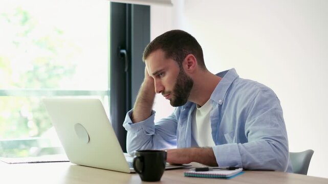 Exhausted and stressed man working on a laptop computer at home, experiencing fatigue and headache from overworking on a difficult project deadline, feeling overwhelmed and frustrated