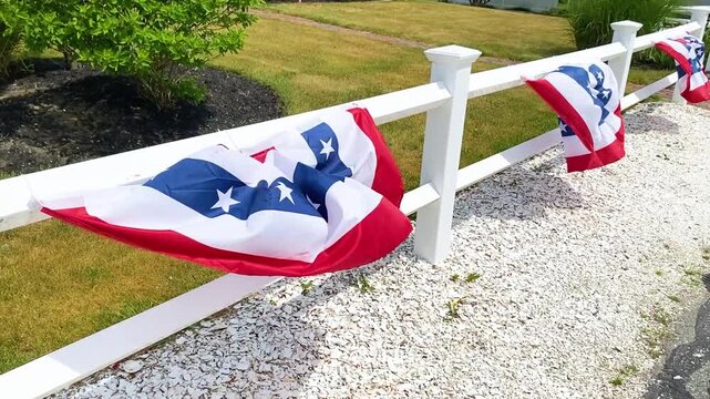 USA bunting flag  attached to a white fence rails swaying on a windy day. Patriotic red white and blue yard decoration for celebrating independence Day or Memorial Day. 