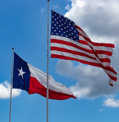 Obraz premium United States and Texas State Flags Waving Proudly Against Blue Sky with Clouds