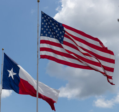 United States and Texas State Flags Waving on Flagpoles Against a Cloudy Blue Sky