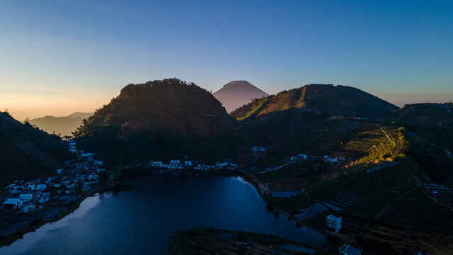Aerial view of Telaga Cebong lake surrounded by terraced hills and volcanic landscape at sunrise in Kejajar, Central Java, Indonesia.