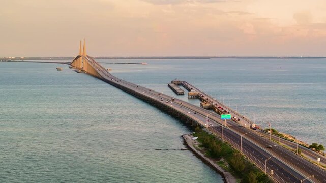 Fishing pier and highway road at sunset. Driving traffic cars on Sunshine Skyway Bridge over Tampa Bay in Florida. Transportation infrastructure in USA