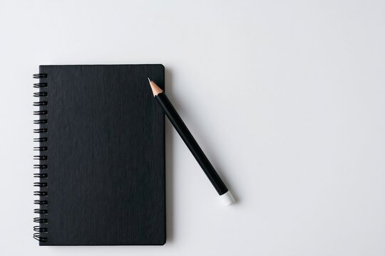 Notebook and black spiral journal with pencil on a minimalist white office desk