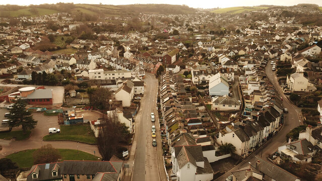 Aerial view of the historic town of Brixham with its dense residential rooftops, winding streets, and surrounding green hills in Brixham, England, United Kingdom.