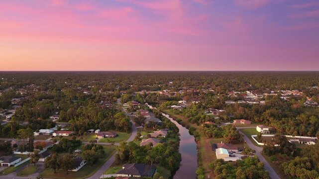 Flood water canal in residential sprawl with scattered homes and streets in sunny Florida at sunset, illustrating land development, infrastructure expansion and suburban lifestyle in the USA.
