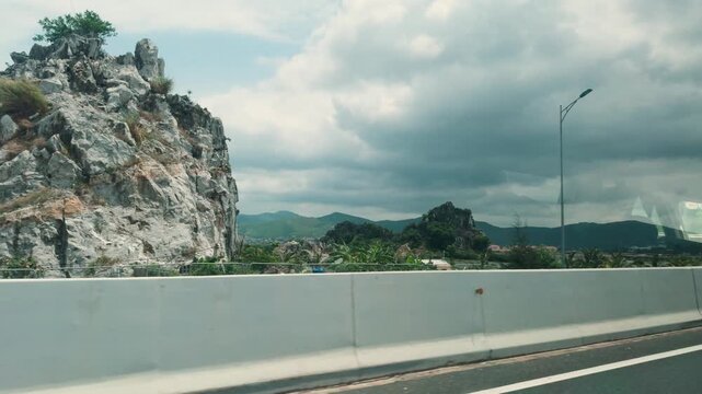 Driving through vietnam's ninh binh province, seeing impressive karst limestone mountains and lush green vegetation alongside the highway under a cloudy sky