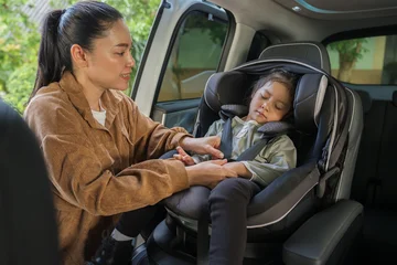 mother is fastening safety belt to preschool child girl while sleeping in car seat, safety baby chair travelling © geargodz