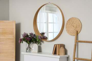 Obraz premium Vase with lilac flowers and books on fireplace near mirror in light room