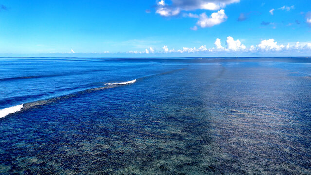 Aerial view of the turquoise Indian Ocean waters, coral reef, and gentle waves breaking off the coast of Trou-aux-Biches, Pamplemousses District, Mauritius.