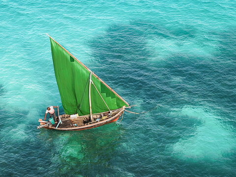Aerial view of a traditional wooden boat with a vibrant green sail navigating through the clear turquoise waters of the Indian Ocean near Vaikaradhoo, Haa Dhaalu City, Maldives.
