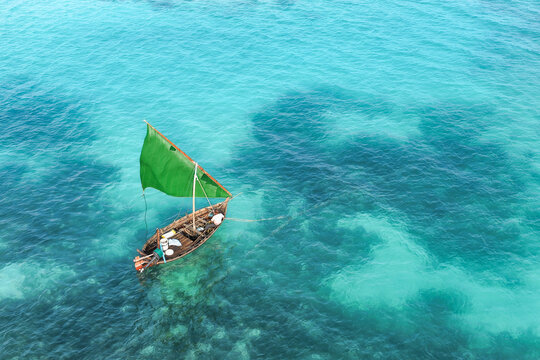 Aerial view of a traditional wooden boat with a vibrant green sail navigating through the clear turquoise waters of the Indian Ocean near Vaikaradhoo, Haa Dhaalu City, Maldives.