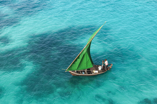 Aerial view of a traditional wooden boat with a vibrant green sail navigating through the clear turquoise waters of the Indian Ocean near Vaikaradhoo, Haa Dhaalu City, Maldives.