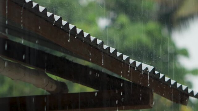 Dramatic rainfall cascading through traditional zinc rooftop, close up water stream and droplets on rustic corrugated iron roof