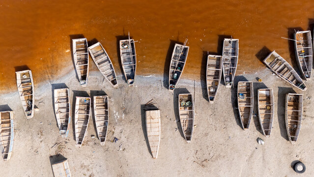 Aerial view of Lake Retba with numerous wooden fishing boats moored on the sandy shore of the pink salt lake in Rufisque, Dakar Region, Senegal.