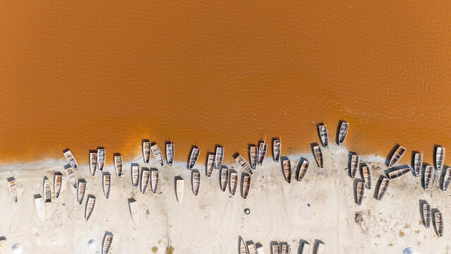 Aerial view of Lake Retba with numerous wooden boats moored along the sandy shore of the pink salt lake in Rufisque, Dakar Region, Senegal.
