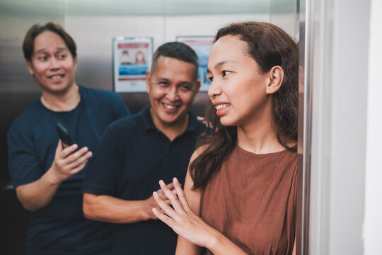 A young asian woman cringes while rebuking advances from two creepy men trying to get her name while inside an elevator. Unwanted attention and uncomfortable scenario.