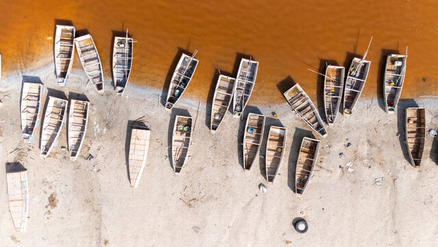 Aerial view of Lake Retba with traditional wooden fishing boats resting on the sandy shore in Rufisque, Dakar Region, Senegal.
