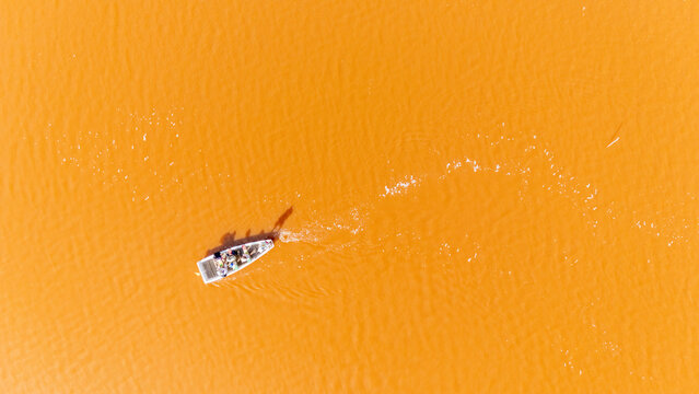 Aerial view of a small boat carrying workers across the vibrant pink waters of Lake Retba in Rufisque, Dakar Region, Senegal.