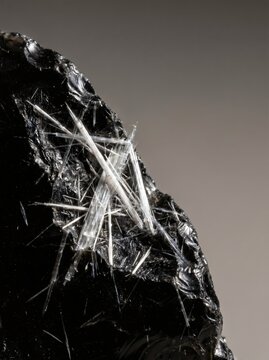 Macro view of sharp white mineral fibers forming on black obsidian rock, geological structure and raw material concept
