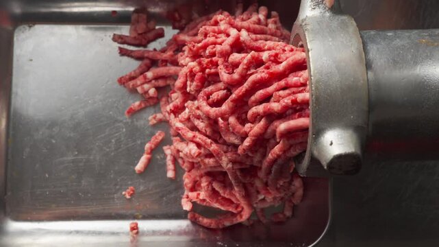 fresh ground beef being processed through a commercial meat grinder in a professional kitchen, top down
