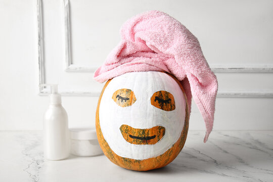 Pumpkin with clay mask, towel and cosmetic products on white grunge table against wooden background