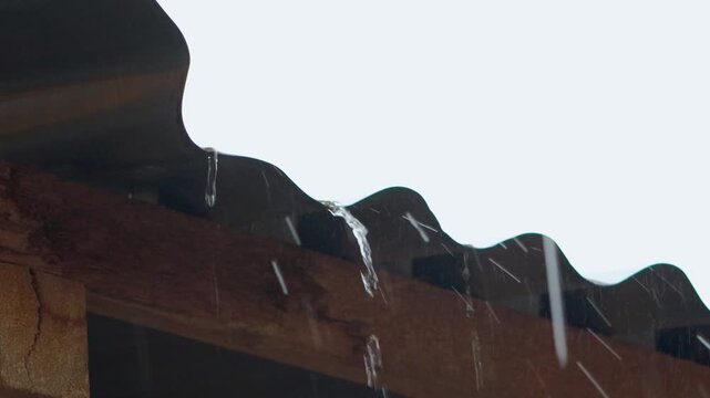 Heavy rain water droplets flowing through zinc metal roof, dramatic rainfall streaming down corrugated iron rooftop
