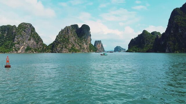 Ha long bay seascape featuring towering limestone karsts covered in lush green vegetation. Reflecting in the calm turquoise waters under a blue sky with scattered clouds