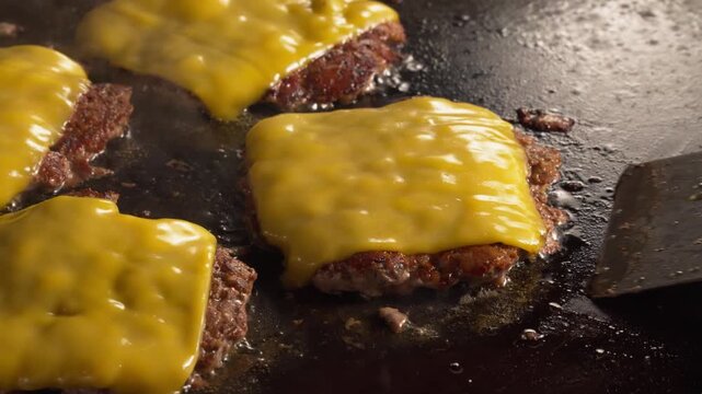 Spatula Lifting juicy smash burger patties topped with melted American cheese sizzling on a hot flat top griddle