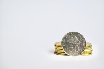 Close-up of a Malaysian 50 sen coin leaning against two small stacks of gold coins, isolated on a clean white background with copy space. © Akram