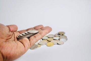 A human palm filled with overlapping silver coins extended over an out-of-focus background of loose cash, illustrating financial transactions and earnings. © Akram