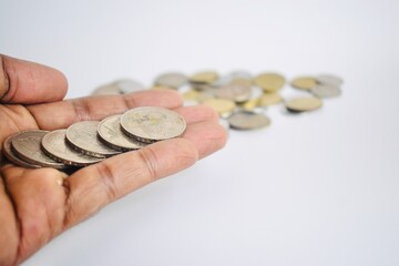 A row of silver coins arranged linearly along a dark-skinned open palm with a blurred pile of change in the background, depicting financial allocation or counting. © Akram