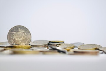 Eye-level view of a standing silver Malaysian coin surrounded by loose pocket change scattered over a clean white background. © Akram