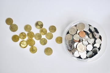 High angle flat lay view of golden Malaysian sen coins neatly organized next to a clear plastic container packed with mixed silver change. © Akram