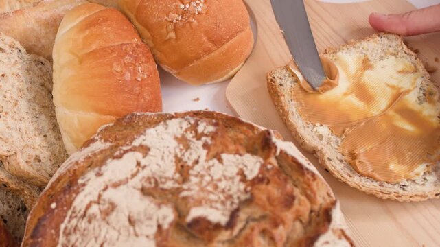Spreading Creamy Peanut Butter on Multigrain Bread Slice with Assorted Loaves