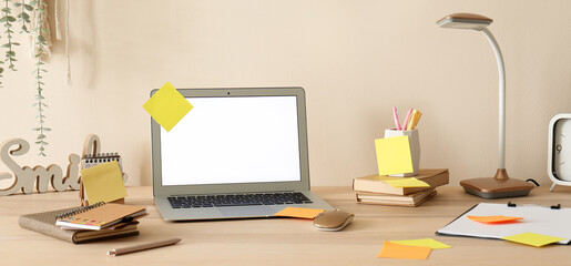 Naklejka premium Blank laptop with sticky notes on desk near beige wall in office