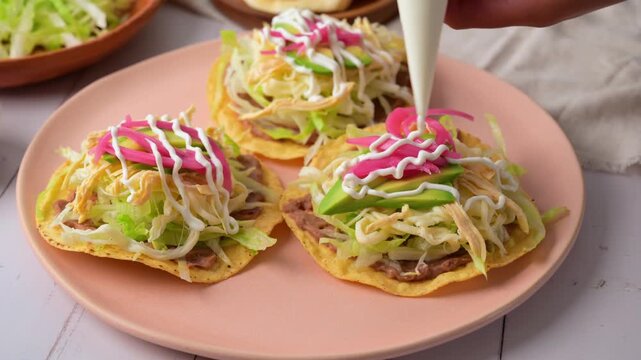 A woman's hand adds Mexican-style cream to a chicken tostada. Mexican food
