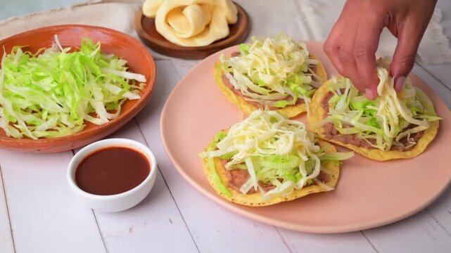 A woman's hand adding Oaxacan string cheese to a tostada. Mexican food. Slow motion