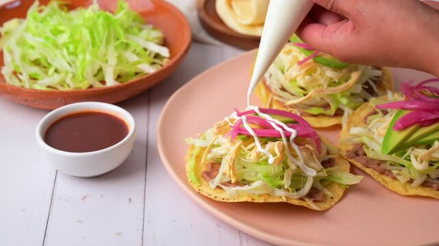 A woman's hand decorating a chicken tostada with Mexican crema. Mexican food