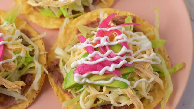 Close up of Mexican tostada topped with shredded chicken, quesillo, cream and pickled onions