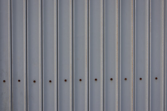close-up, full-frame shot of a gray corrugated metal sheet with a row of rusty bolts.
