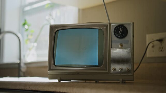 Cinematic slow pan across a cracked ceramic tile kitchen table with a dusty small CRT television displaying flickering white noise. Chipped walls and rusty fixtures visible.