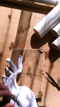 A curator prepares to inspect a fragile vintage notebook by carefully putting on archival gloves. Footage conveys preservation, historical research, and professional conservation practices.