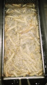 Vertical video. French fries. Hot fryer. Professional industry heat kitchen equipment. Metal container basket for cooking potato in oil.