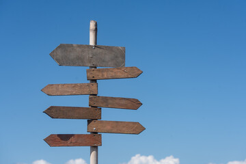 Wooden signpost with blank arrows pointing in different directions against a clear blue sky © Dontree