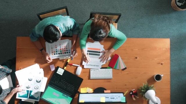 Top view of project manager writing idea while team joining meeting and talking about idea. Professional designer design logo while looking at color palette and writing idea down in paper. Symposium.